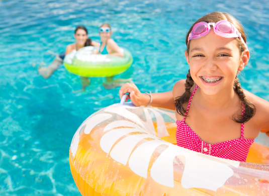 A girl in the pool with an orange and white float.